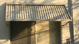 Residential corrugated metal tan window awnings.