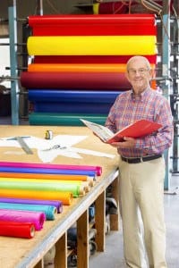 Owner of Goodwin-Cole standing in front of rolls of fabic while holding a book