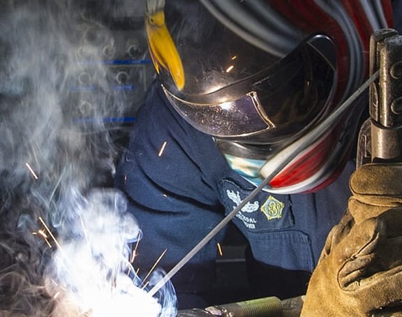 Person welding in blue overalls with mask on